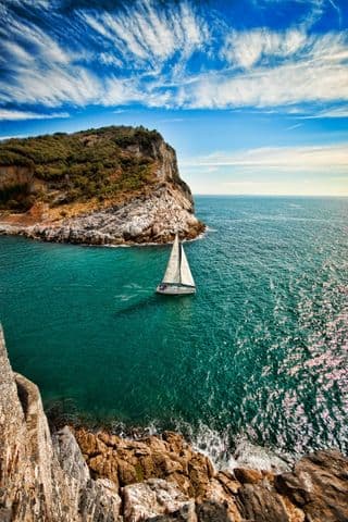 Sailboat Navigating the Emerald Waters near Rocky Coastline