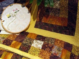 Embroidery Hoop with Floral Design Next to Patchwork Quilt